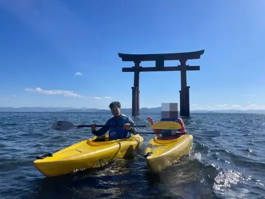 滋賀県の白鬚神社の湖中大鳥居を背景に、琵琶湖でカヤックに乗る田畑雄貴