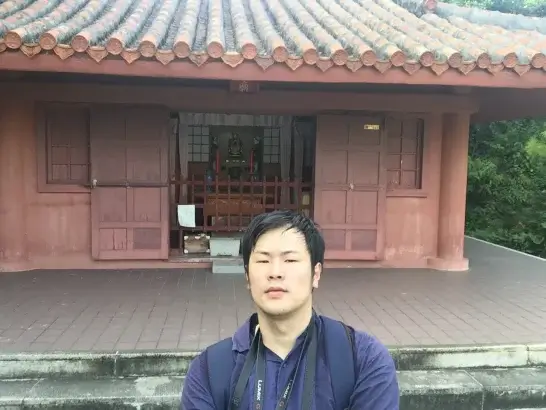 沖縄県那覇市若狭の天尊廟を訪れた田畑雄貴。赤瓦の廟と祭壇を背景に撮影