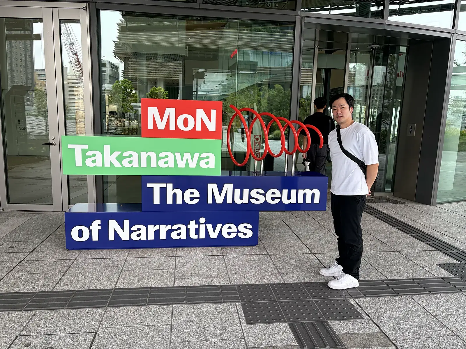 いのちの未来+の会場、MoN Takanawaの入口のロゴの前に立つおとぼけ