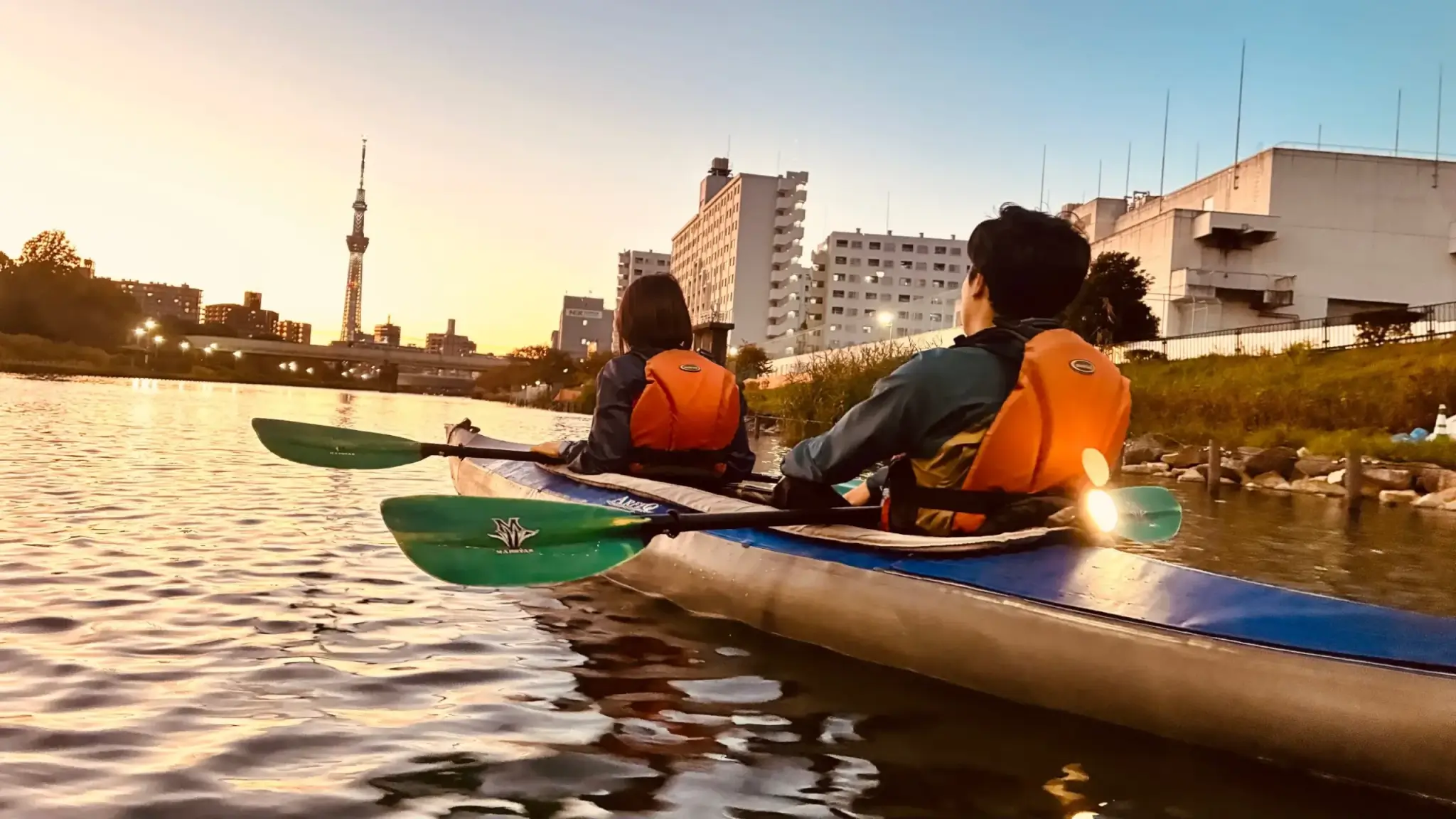 夕焼けの旧中川をカヤックで進みながら、正面の東京スカイツリーを眺める2人